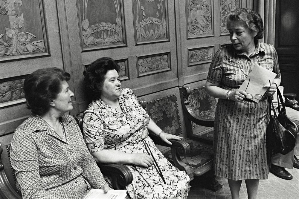 Auf der hintersten Stuhlreihe des Nationalratssaals sitzen die Nationalrätinnen Liselotte Spreng und Hedi Lang in ein Gespräch mit der stehenden Elisabeth Blunschy vertieft. Aufgenommen 1980.