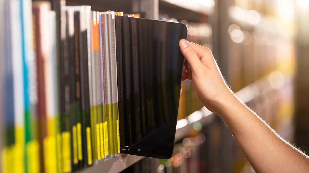 Auf dem Bild sieht man eine Hand, die eine Tablet aus dem Regal holt.