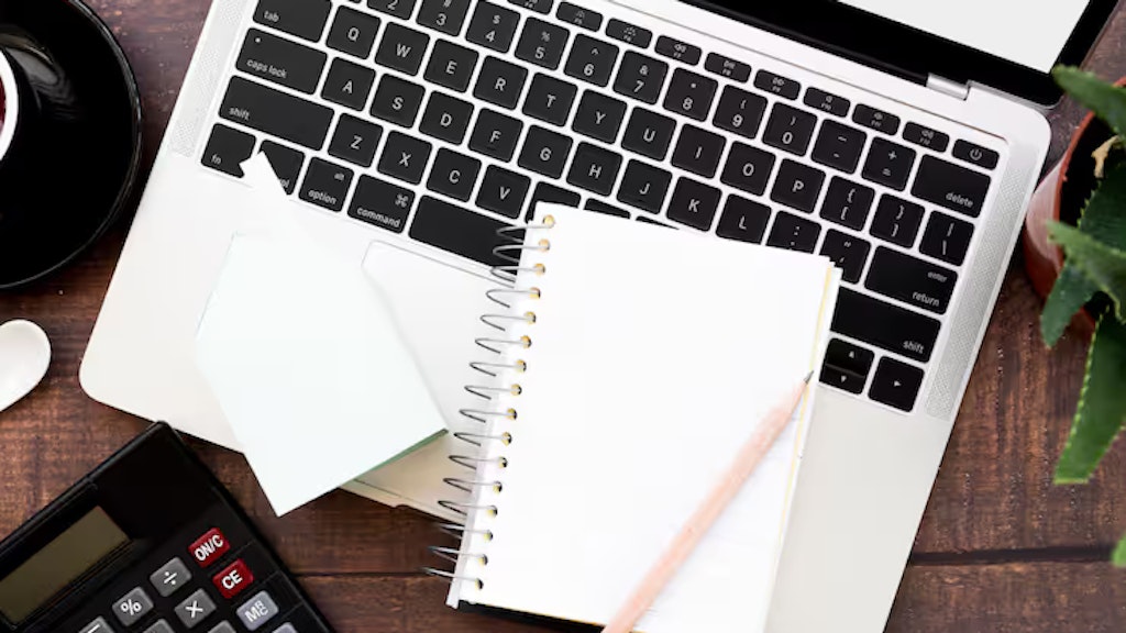 Carnet vierge enroulé avec un crayon sur un ordinateur portable ouvert posé sur une table en bois