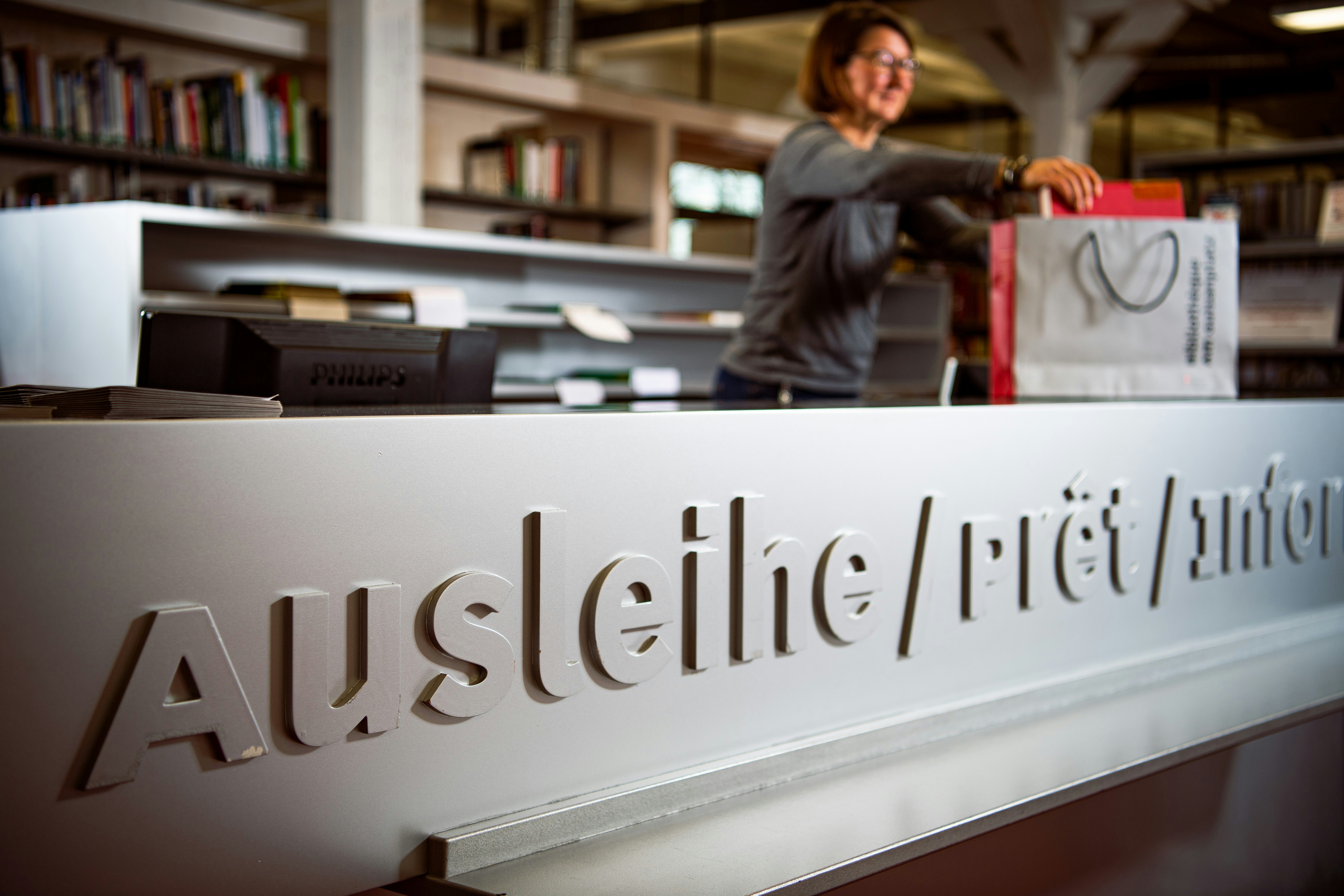 Eine Bibliotheksmitarbeiterin packt neu ausgeliehene Bücher in eine Tasche ein. Sie steht an der Ausleihtheke der BiG. (Bild: ZEM_ Sina Guntern/ZEM)