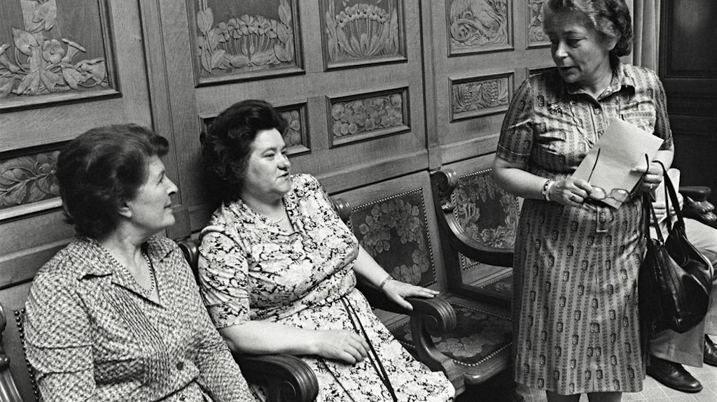 Auf der hintersten Stuhlreihe des Nationalratssaals sitzen die Nationalrätinnen Liselotte Spreng und Hedi Lang in ein Gespräch mit der stehenden Elisabeth Blunschy vertieft. Aufgenommen 1980.