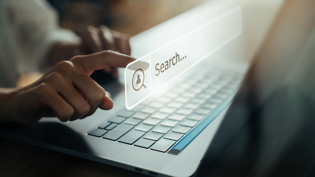 Auf dem Bild sieht man eine Hand die den Laptop benutzt und auf den Bildschirm zeigt, um online im Internet zu surfen.
