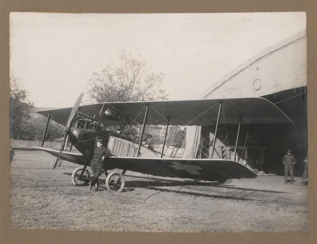 Das Bild zeigt Soldaten der Fliegertruppen mit einem Flieger vor einem Hangar im Aarauer Schachen, aufgenommen ca. 1914. Auf der Unterseite der Flügel sind Schweizer Kreuze aufgemalt, damit die Flugzeuge nicht versehentlich beschossen wurden. (aus: Hans Bandi (vermutlich). Photos aviation dès 1914, BIG DU 555)